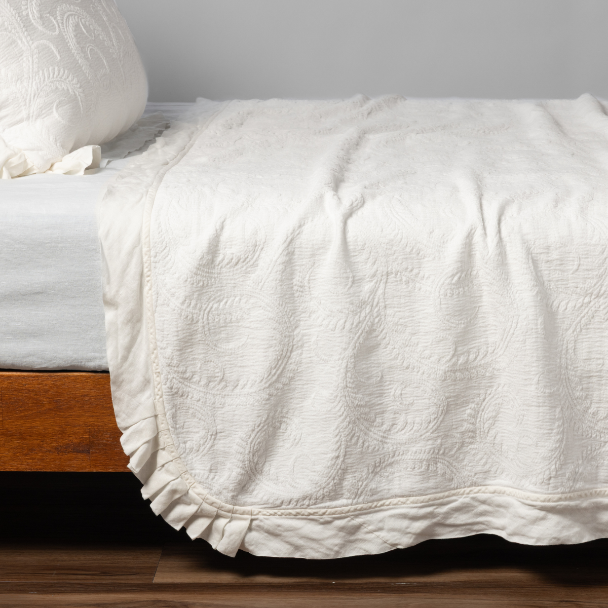 Marisette Bedspread | Winter White | matching organic cotton damask trimmed with linen bedspread and sham on a bed with white fitted sheet, shown from the side against a plain background.