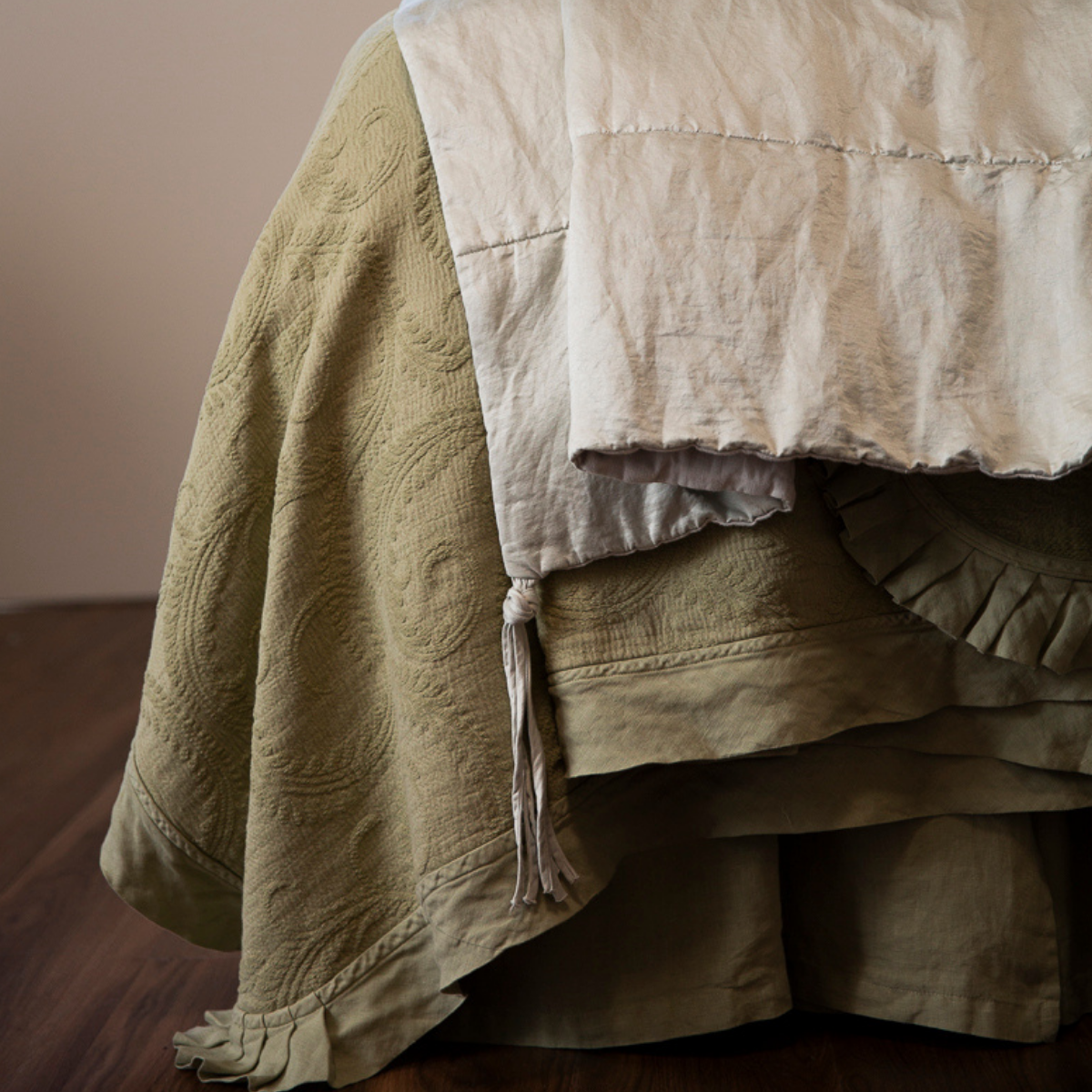 Marisette Bedspread | a close up of the ruffle and pleated corner of a green oversized coverlet with a tasseled throw blanket layered on top.