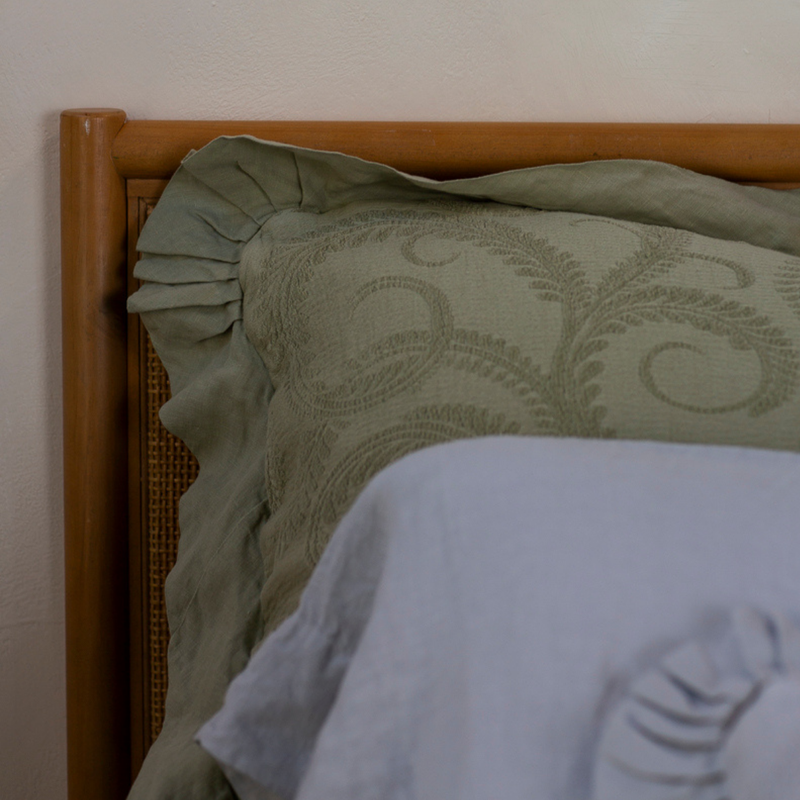Marisette Sham | the corner of an organic cotton damask sham against a rattan headboard with a sleeping pillow in the foreground.