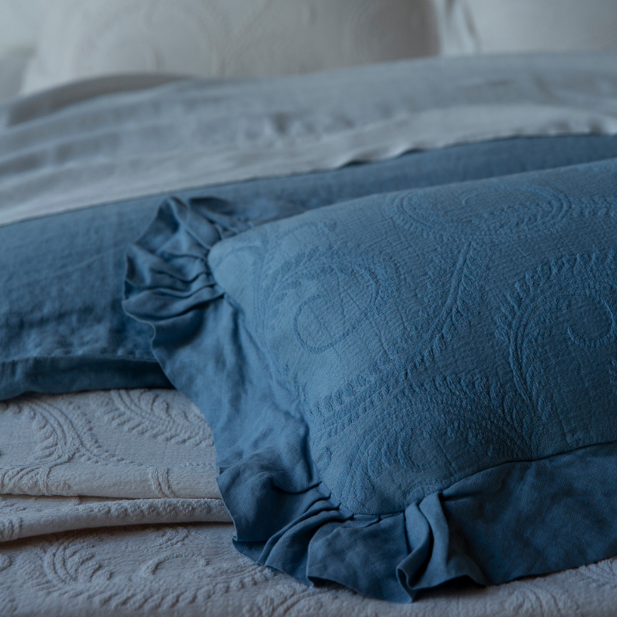 Marisette Throw Pillow | [allvaariants] | close-up of throw pillow in organic cotton damask with linen trim in tahoe blue with other blue bedding.