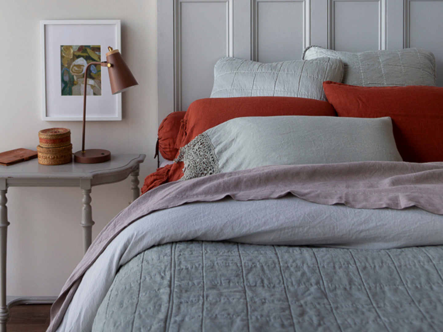 A lightly dressed bed that mixes our existing fabrics with our new Sel collection. A pop of Autumn sits against an earthy-toned bed. Light gray bed sore-able with brown decor ontop sits next to the bed. 