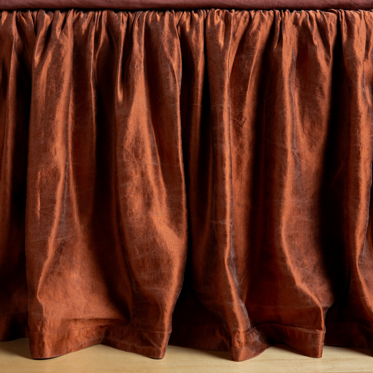 Autumn | A close-up side view of a bed with the Paloma bed skirt in Autumn, a rich terracotta tone.