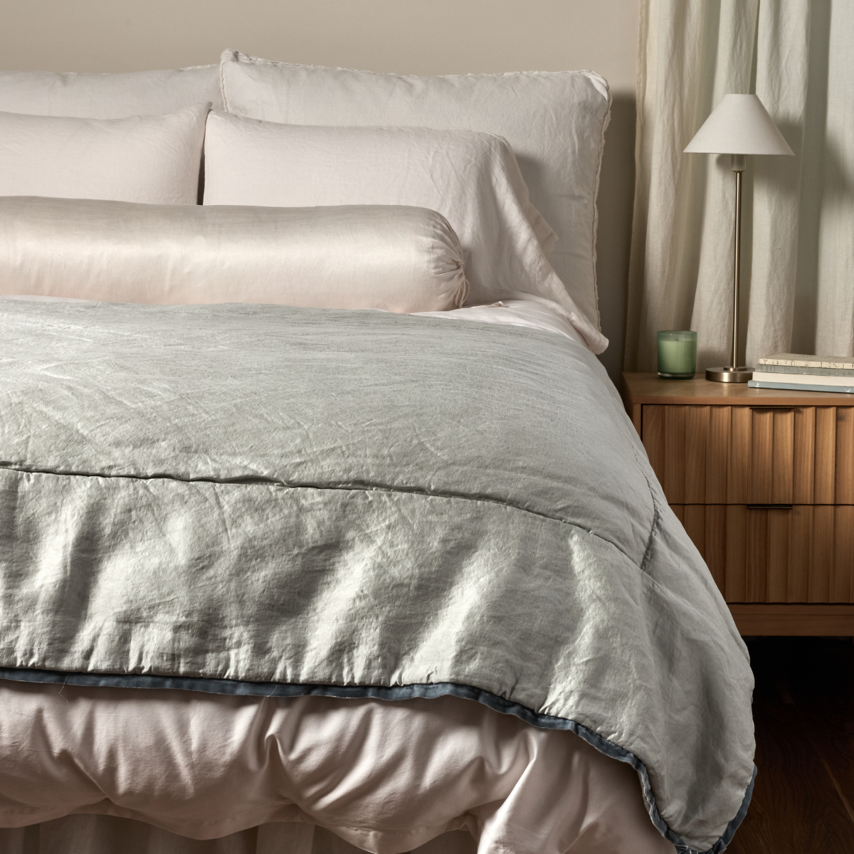 Paloma Blanket | Cloud | a charmeuse bed end blanket is shown layered at the foot of a bed, its contrasting silk velvet trim and petit ruffle at the corner visible against the all winter white bedding.