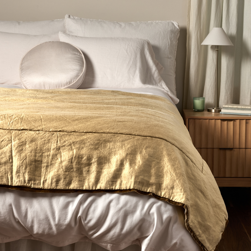 Paloma Blanket | Honeycomb | a charmeuse bed end blanket is shown layered at the foot of a bed, its contrasting silk velvet trim and petit ruffle at the corner visible against the all winter white bedding.