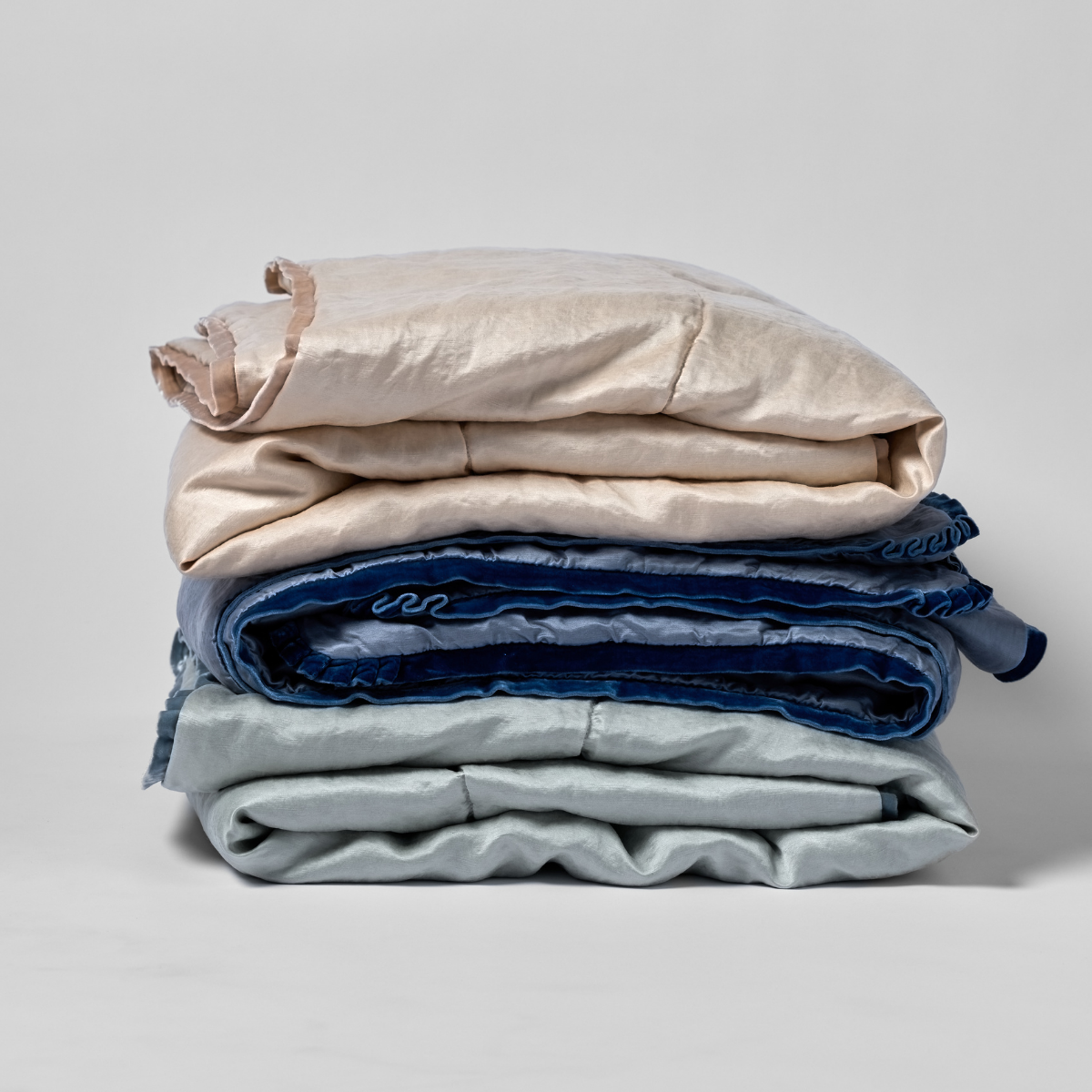 Paloma Blanket | a stack of three folded charmeuse blankets in pearl, tahoe blue, and cloud shown against a white background.