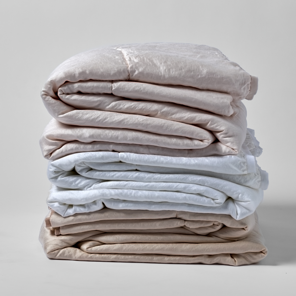 Paloma Blanket | a stack of three folded charmeuse blankets in blush, white, and pearl shown against a white background. 