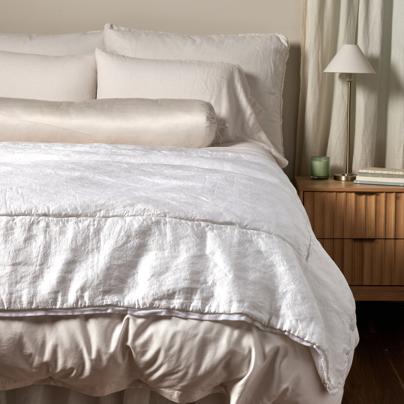 Paloma Blanket | White | a charmeuse bed end blanket is shown layered at the foot of a bed, its contrasting silk velvet trim and petit ruffle at the corner visible against the all winter white bedding.