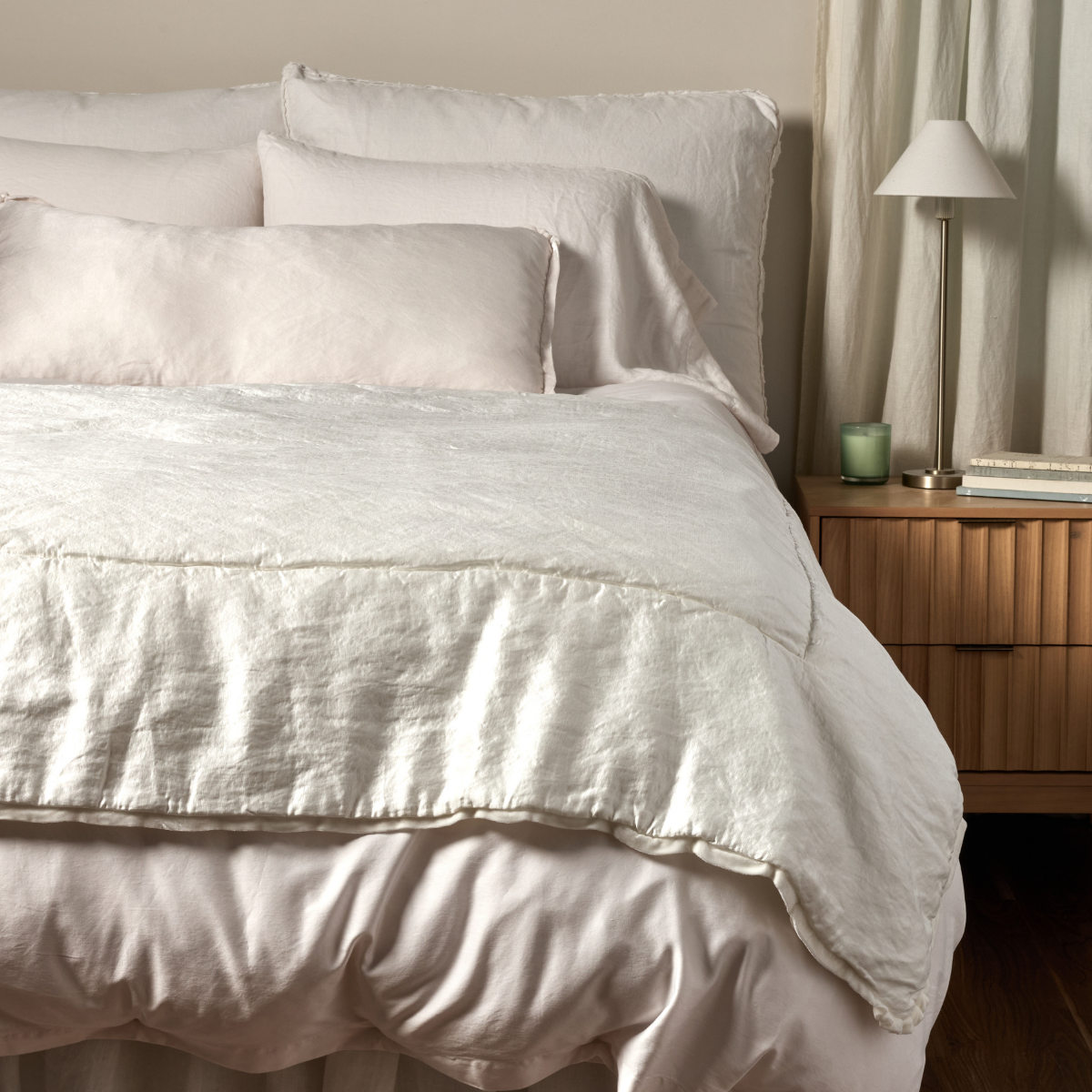 Paloma Blanket | Winter White | a charmeuse bed end blanket is shown layered at the foot of a bed, its subtle silk velvet trim and petit ruffle at the corner visible against the all winter white bedding.