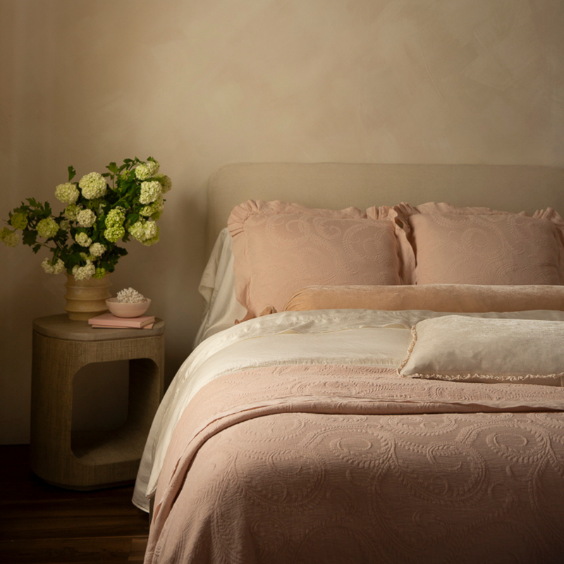 Marisette Bedspread | a pink and neutral toned bed with flowers on the side table against a neutral limewash wall and moody lighting