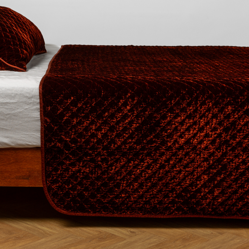 Autumn | A close-up side view of a bed with our Silk Velvet Quilted coverlet and a matching pillowcase in Autumn, a rich terracotta tone.