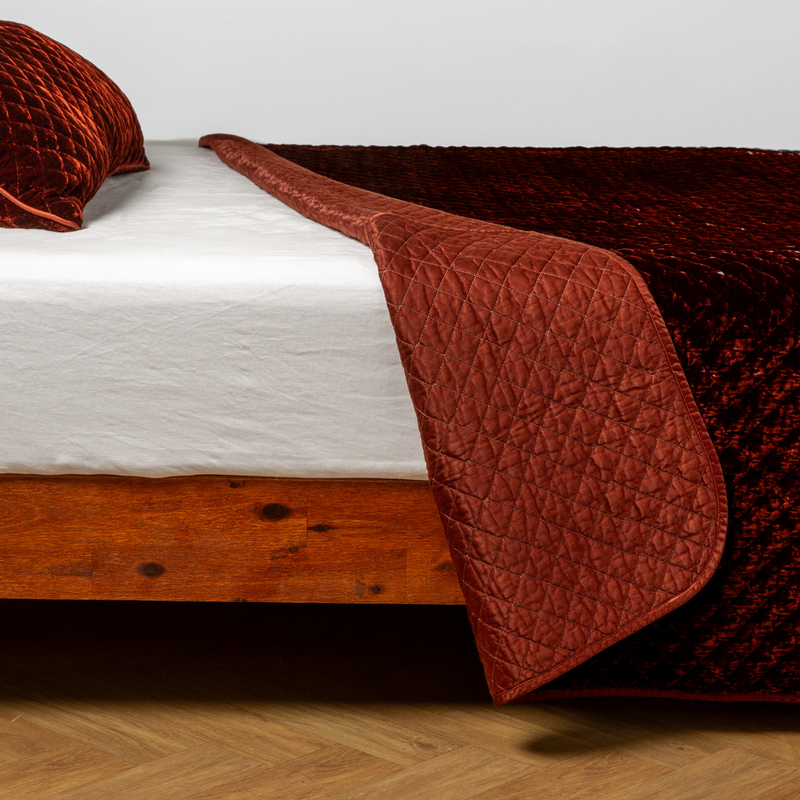 Autumn | A close-up side view of a bed with our Silk Velvet Quilted Coverlet and a matching pillowcase in Autumn, a rich terracotta tone.