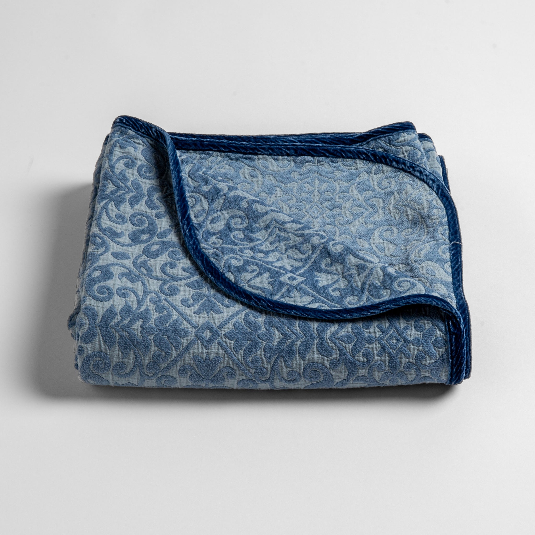 Vienna Baby Blanket | Tahoe Blue | a folded cotton chenille baby blanket trimmed in silk velvet shot overhead at a slight angle against a white background.