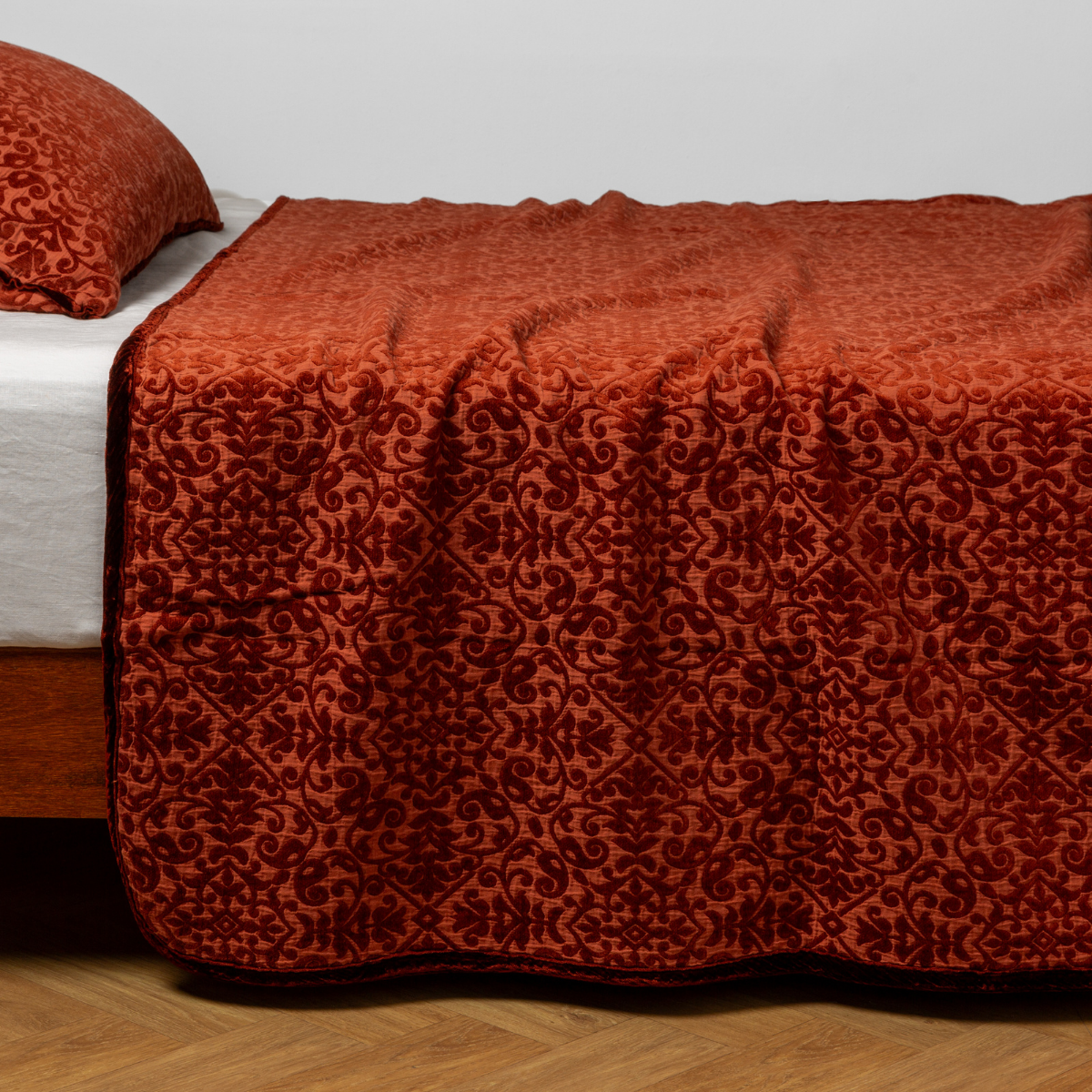 Vienna Twin Coverlet | Autumn | A close-up side view of a bed with our Vienna coverlet and a matching pillowcase in Autumn, a rich terracotta tone.