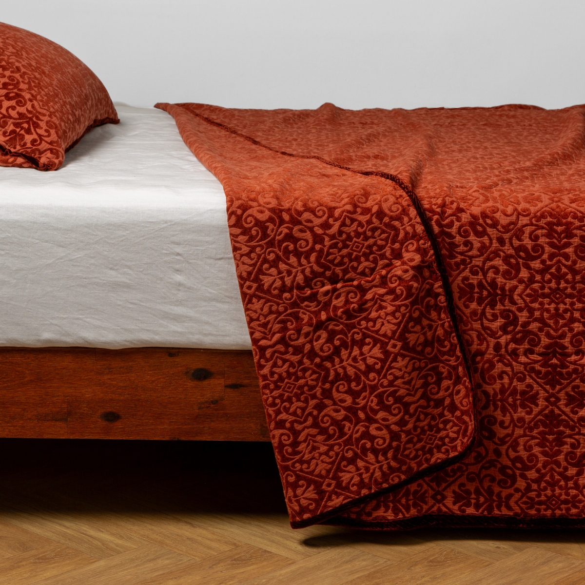 Vienna Twin Coverlet | Autumn | A close-up side view of a bed with our Vienna coverlet and a matching pillowcase in Autumn, a rich terracotta tone.