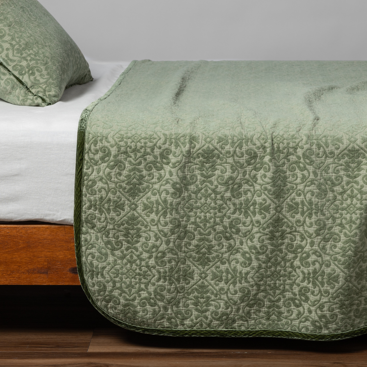 Desert Sage | matching vienna coverlet and sham in desert sage, a serenely elegant green, offering a hushed hue, shown from the side on a bed against a plain background.