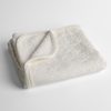 Adele Baby Blanket | Winter White | a folded blanket with the corner turned down to show the trim against a white background, shot from an overhead angle.