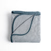 Adele Blanket | Mineral | folded organic cotton damask throw blanket shown with the corner folded down to show silk velvet trim detail — overhead against a plain white background.