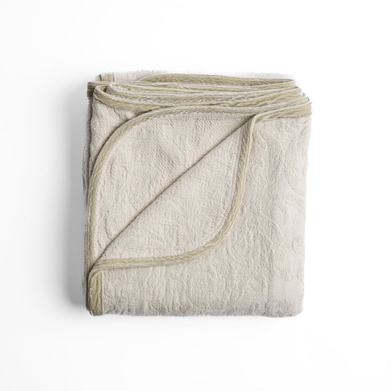Adele Blanket | Parchment | folded organic cotton damask throw blanket shown with the corner folded down to show silk velvet trim detail — overhead against a plain white background.