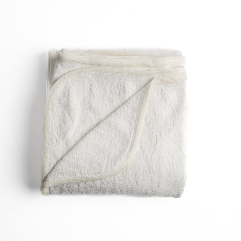 Adele Blanket | Winter White | folded organic cotton damask throw blanket shown with the corner folded down to show silk velvet trim detail — overhead against a plain white background.