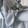 Cloud | A close up of the Adele baby blanket in cloud draped over a crib mattress, highlighting the texture of the cotton damask and the silk velvet edging. The trim absorbs the dye more richly than the cotton body.