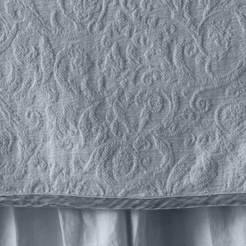 Cloud | Close up of the Adele coverlet in cloud, highlighting the detail of the cotton damask and the silk velvet edging trim. A white bed skirt peeks out at the bottom of the shot.