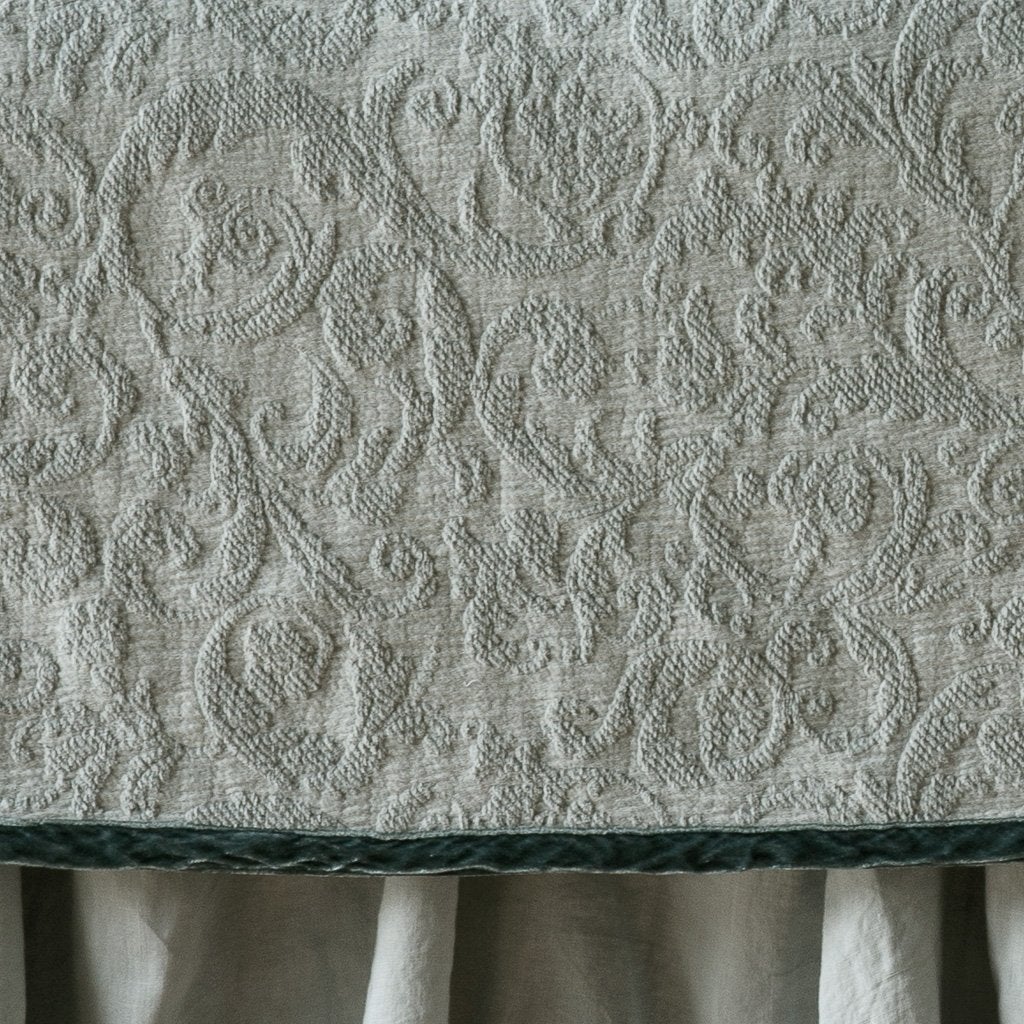 Eucalyptus | Close up of the Adele coverlet in eucalyptus, highlighting the detail of the cotton damask and the silk velvet edging trim. A white bed skirt peeks out at the bottom of the shot.