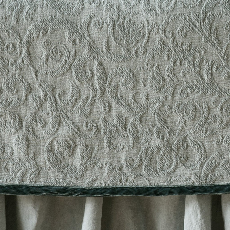 Eucalyptus | Close up of the Adele coverlet in eucalyptus, highlighting the detail of the cotton damask and the silk velvet edging trim. A white bed skirt peeks out at the bottom of the shot.