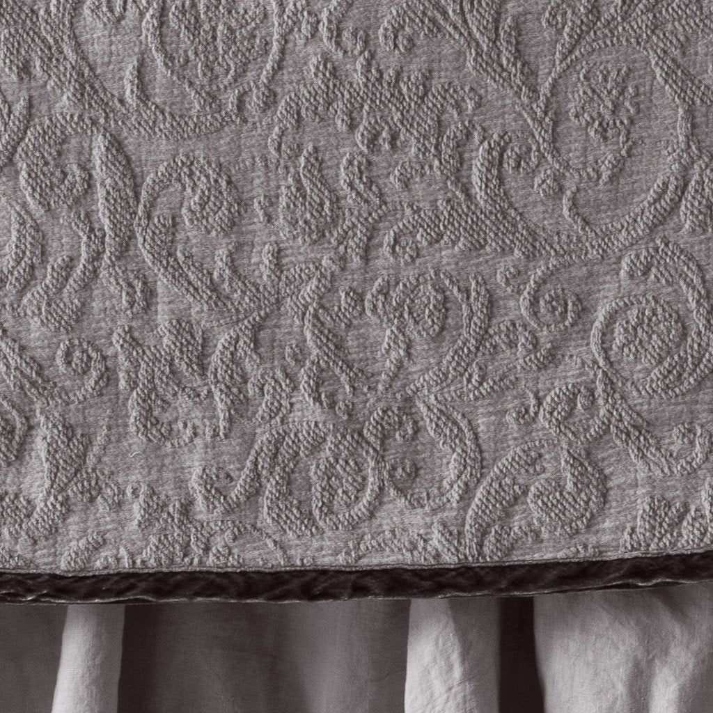 Fog | Close up of the Adele coverlet in fog, highlighting the detail of the cotton damask and the silk velvet edging trim. A white bed skirt peeks out at the bottom of the shot.