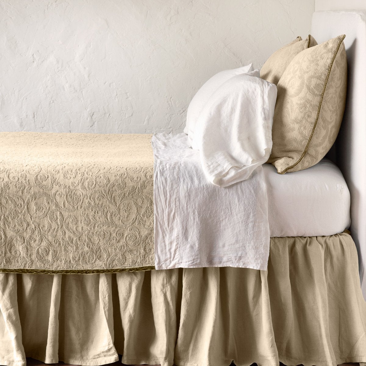 Honeycomb | The Adele coverlet in honeycomb, on a bed viewed from the side against a plain white wall. The bed is styled neatly with the coverlet folded back to reveal white sheets, bed skirt and pillows.
