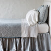 Adele Twin Coverlet | Mineral | The Adele coverlet in mineral, on a bed viewed from the side against a plain white wall. The bed is styled neatly with the coverlet folded back to reveal white sheets, bed skirt and pillows.