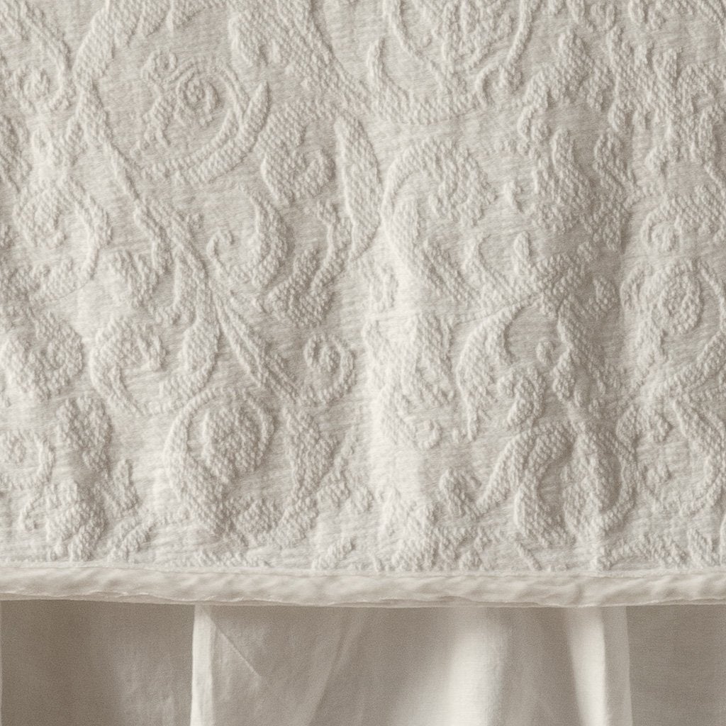Parchment | Close up of the Adele coverlet in parchment, highlighting the detail of the cotton damask and the silk velvet edging trim. A parchment bed skirt peeks out at the bottom of the shot.
