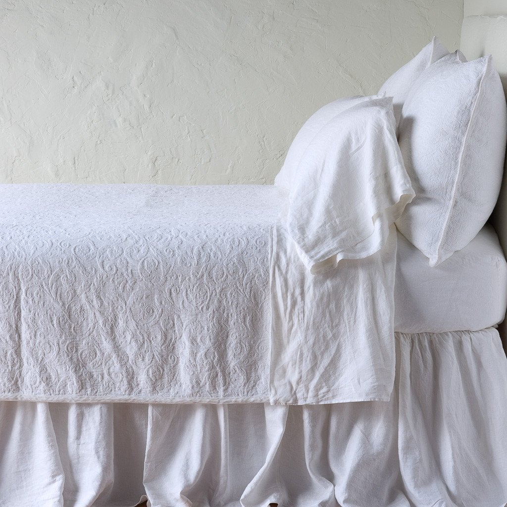 White | The Adele coverlet in white, on a bed viewed from the side against a plain white wall. The bed is styled neatly with the coverlet folded back to reveal white sheets, bed skirt and pillows.