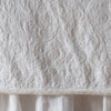 Winter White | Close up of the Adele coverlet in winter white, highlighting the detail of the cotton damask and the silk velvet edging trim. A winter white bed skirt peeks out at the bottom of the shot.