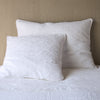 White | Two Adele shams in white, shown in euro and deluxe sizes, leaning against a neutral toned headboard on white bedding.