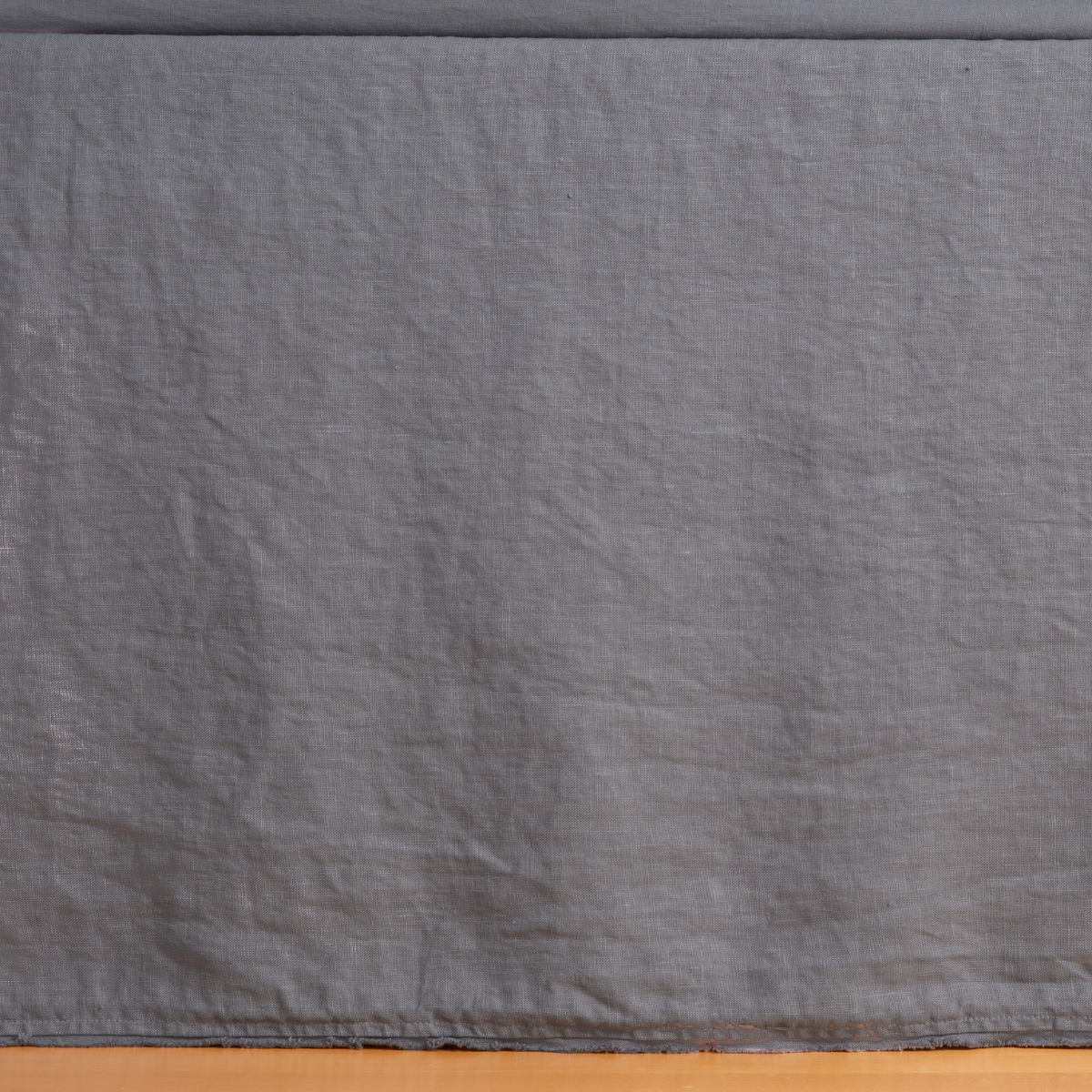 Austin Bed Skirt | French Lavender | a close up of a midweight linen bed skirt  barely touching a warm wooden floor.