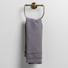Austin Guest Towel | French Lavender | midweight linen guest towel with raw edge band at both ends hanging from a towel ring mounted to a white wall.