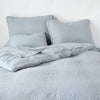 Austin duvet cover shown with one corner folded back from foot of bed angle. Bedding is monochromatic soft blue grey tone.