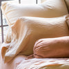 Close up of Austin sham leaning against a black framed window, layered behind shimmery silk charmeuse pillows.