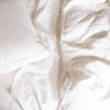 Austin sham with linen sheets and pillows in monochromatic white. Overhead close up angle highlights the raw-edge trim detail on the sham gusset.