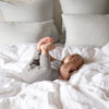 Baby laying in a playful pose on a rumpled bed with Austin shams in the background.