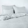 Austin Sham | Cloud | Midweight linen shams shown from foot of bed, leaning against a plain background with monochromatic bedding.
