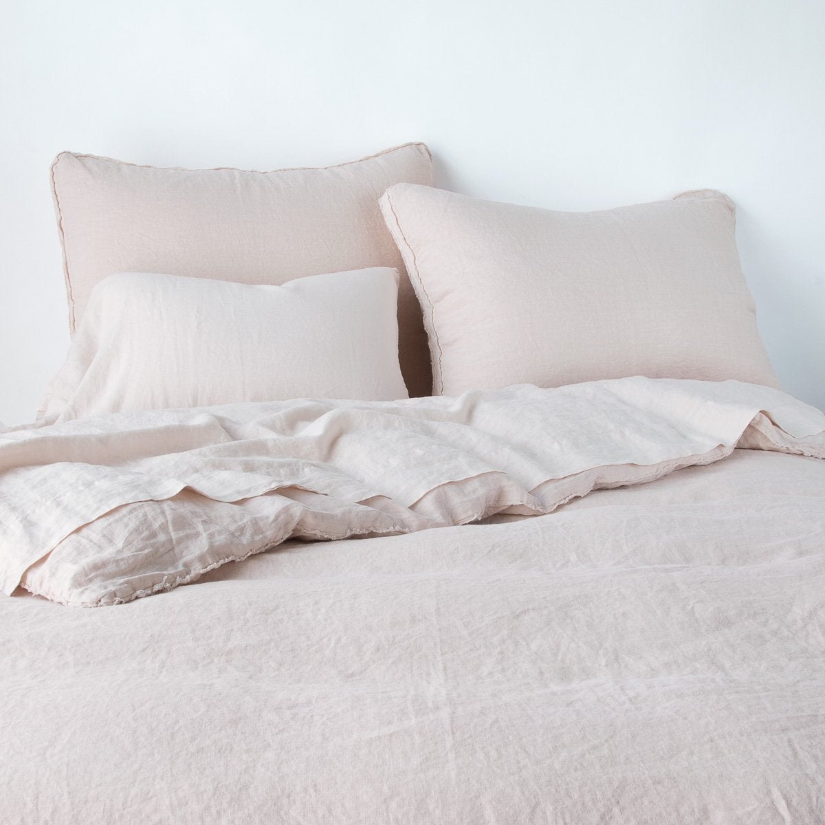 Austin Sham | Pearl | Midweight linen shams shown from foot of bed, leaning against a plain background with monochromatic bedding.