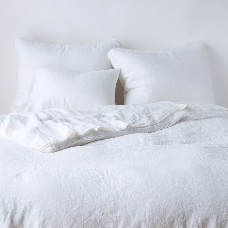 Austin Sham | White | Midweight linen shams shown from foot of bed, leaning against a plain background with monochromatic bedding.