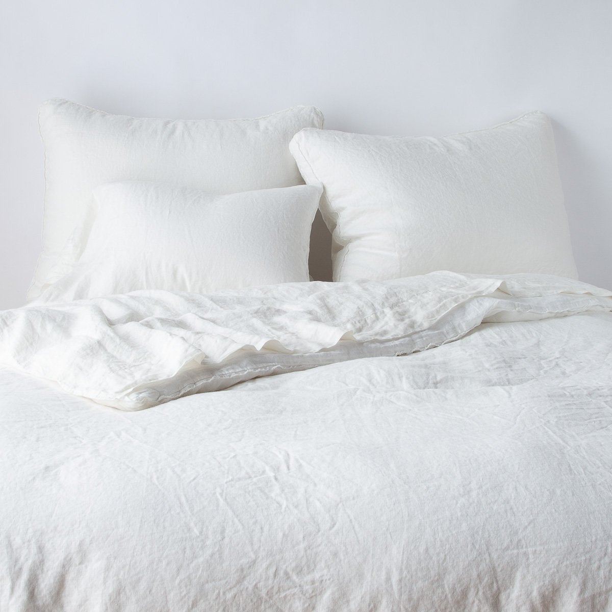 Austin Sham | Winter White | Midweight linen shams shown from foot of bed, leaning against a plain background with monochromatic bedding.