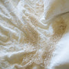 Close up of a Frida flat sheet and pillowcase, layered over embroidered silk velvet, all in winter white - overhead view.