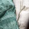Close-up of Ines duvet cover in jade against light linen sheets, showcasing the embroidery pattern detail - overhead view.