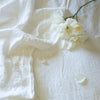 Linen Flat Sheet | Linen fitted and flat sheets in light cream tone with scattered white flowers and petals - overhead view.