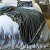 Linen Whisper bed skirt in cloud, layered under a matching duvet cover and mineral silk velvet accessory pieces - end of bed view.