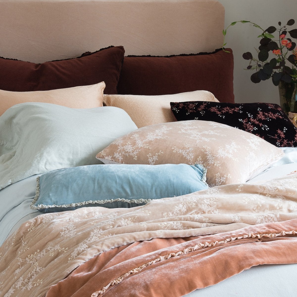 Lynette Blanket | Pearl | Lynette throw blanket and throw pillow in pearl, layered on rumpled bed with pink, pale blue, and rich brown tones - cropped three-quarter angle.