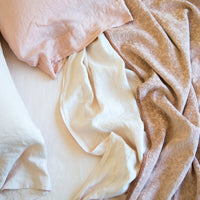 [allvariants]: Close-up of rumpled Vienna coverlet with linen sheets and sleeping pillows - in pink and cream tones - overhead view.